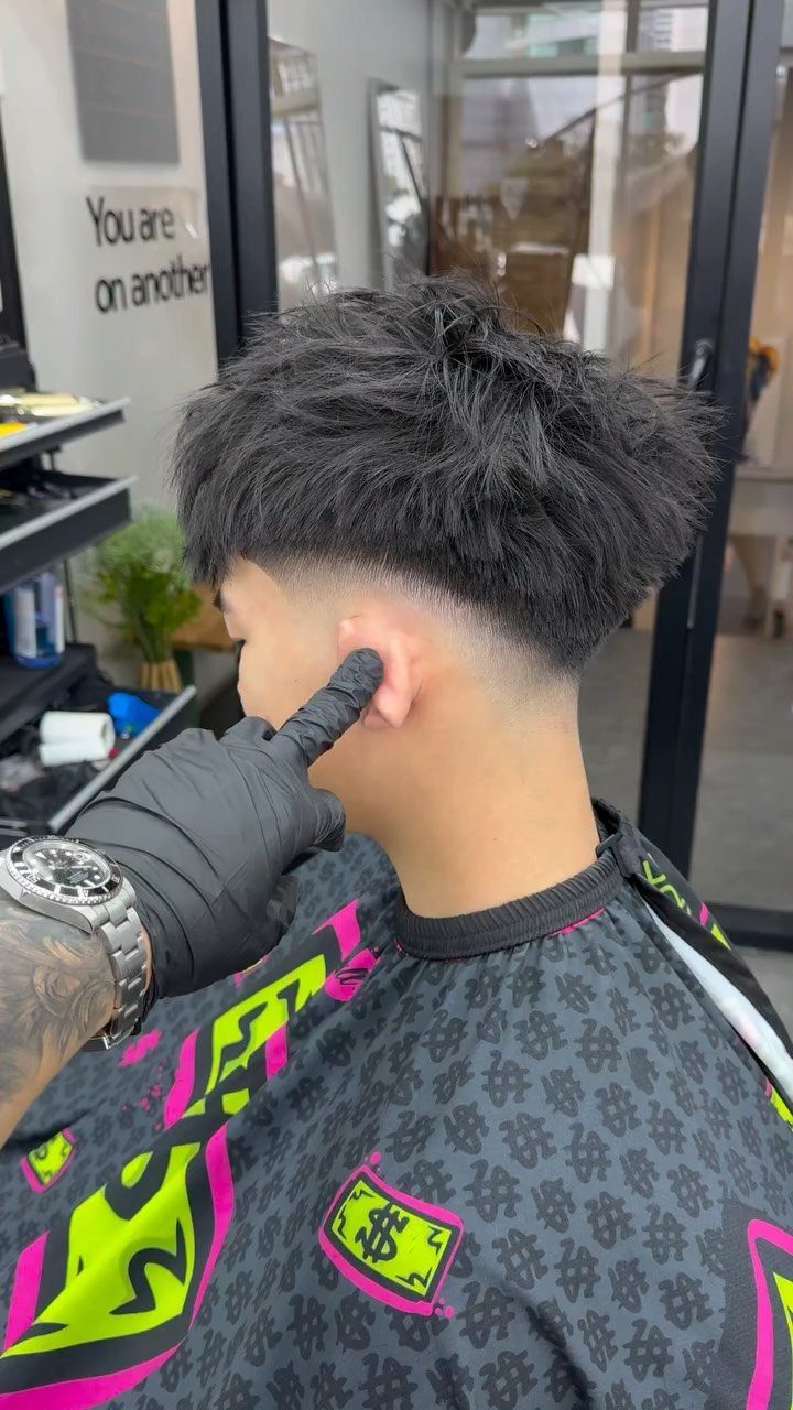 Man with messy black hair and low drop taper fade in a barbershop.