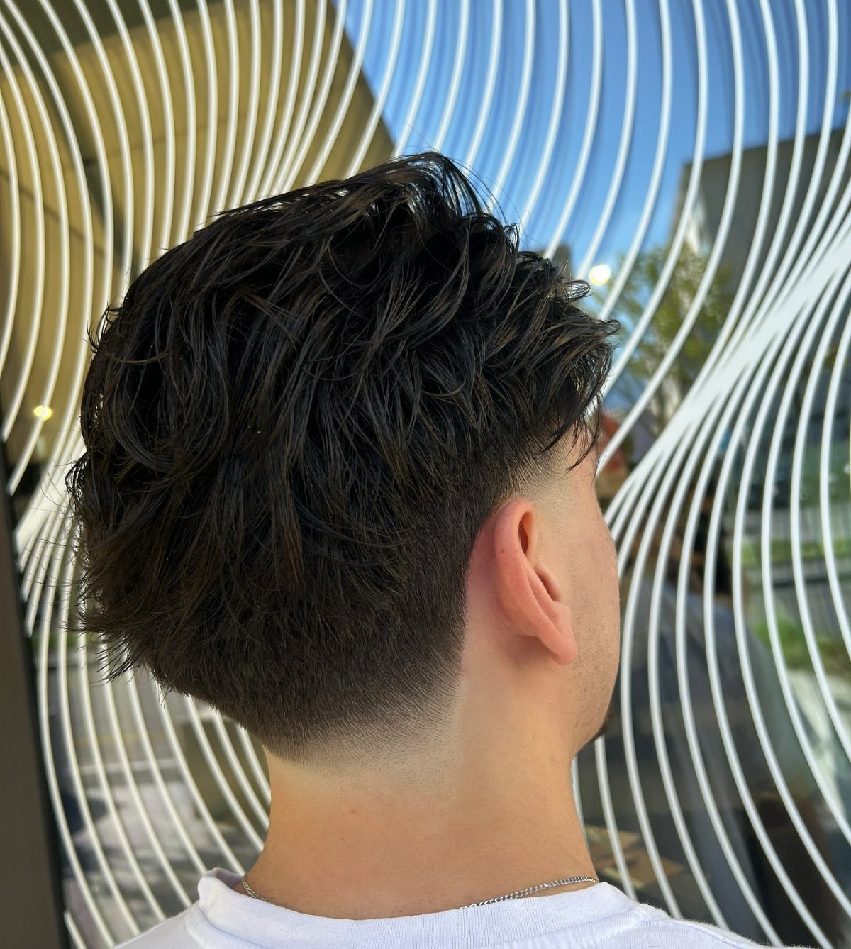 Man with dark wavy hair and a low fade haircut from the side.