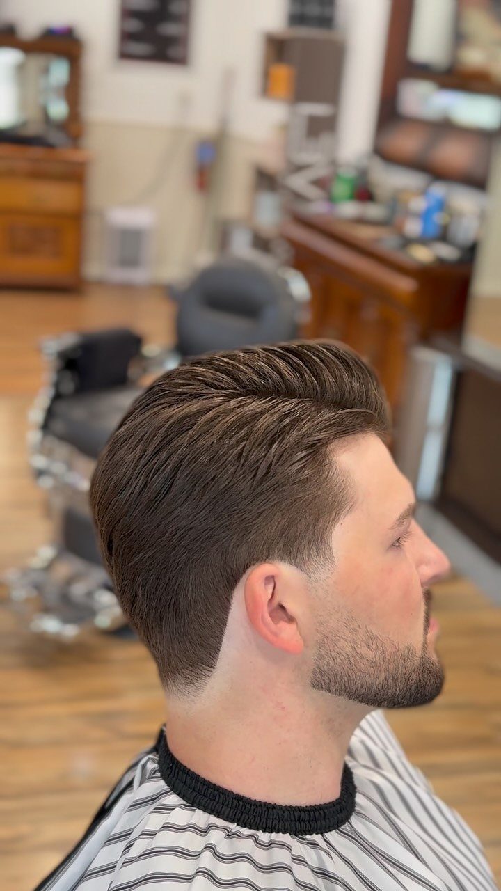 Man with a side part hairstyle and a low taper fade in a barbershop.