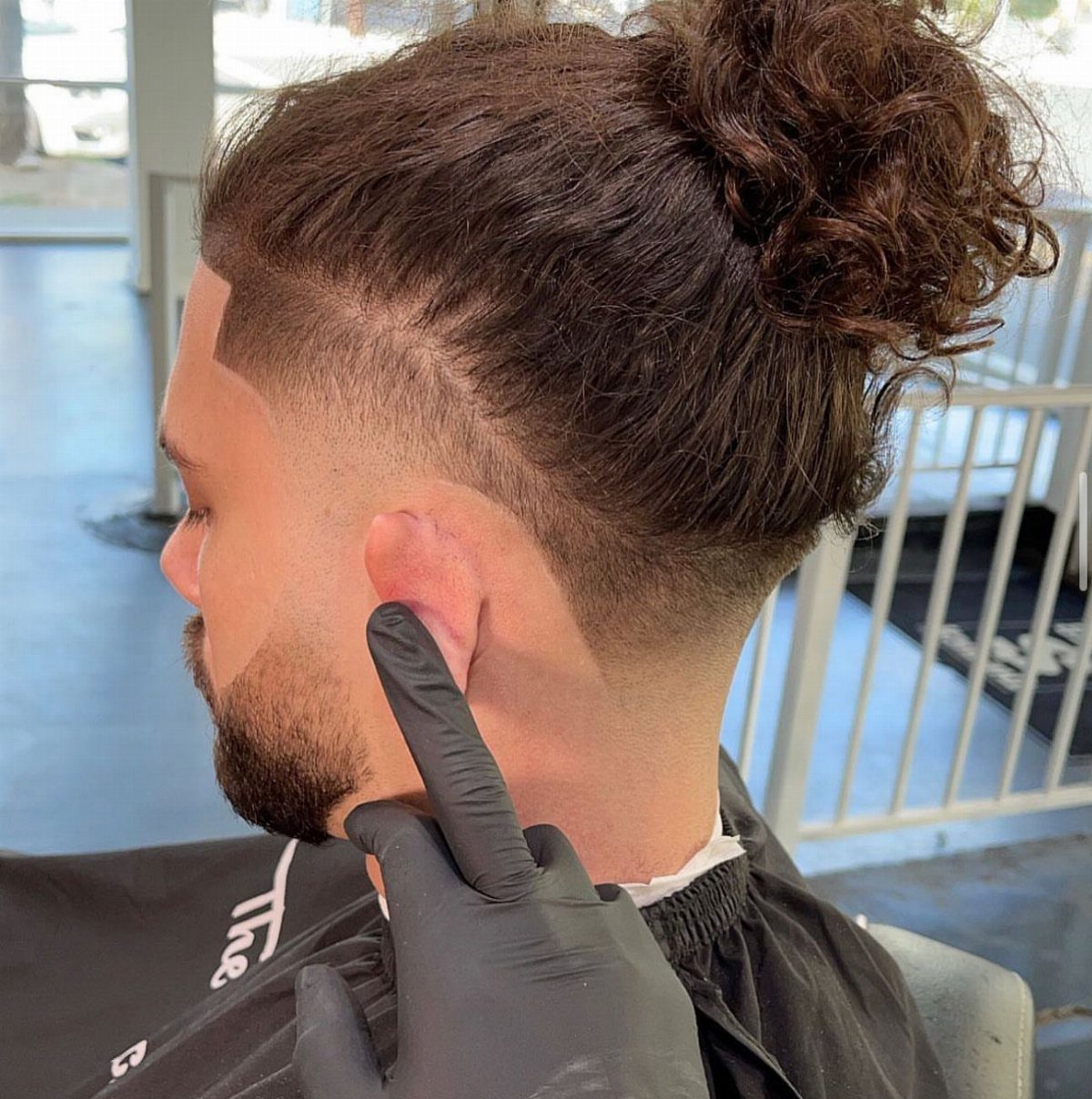 Man with curly hair bun and low taper faded undercut at a barbershop