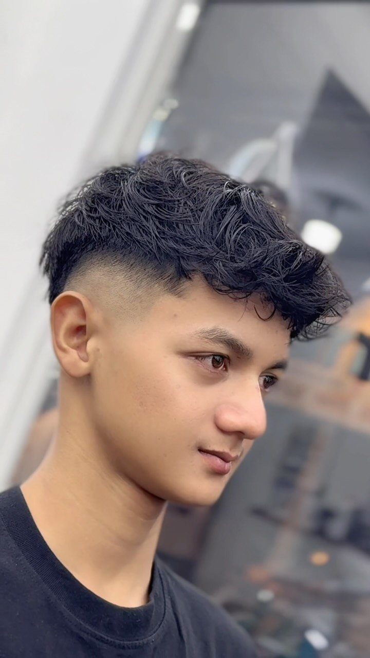 Young man with curly top hair and a clean mid fade haircut.