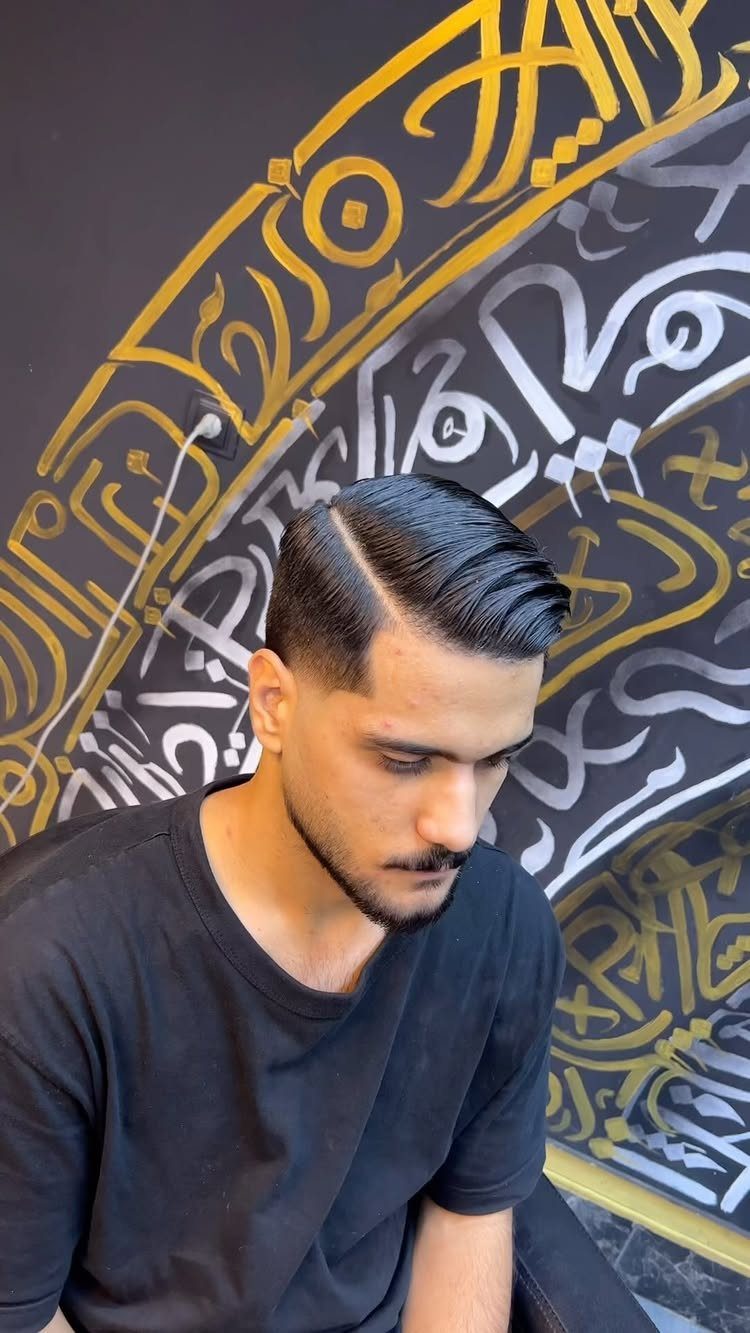 Man with a side parting fade haircut and beard against calligraphic wall.