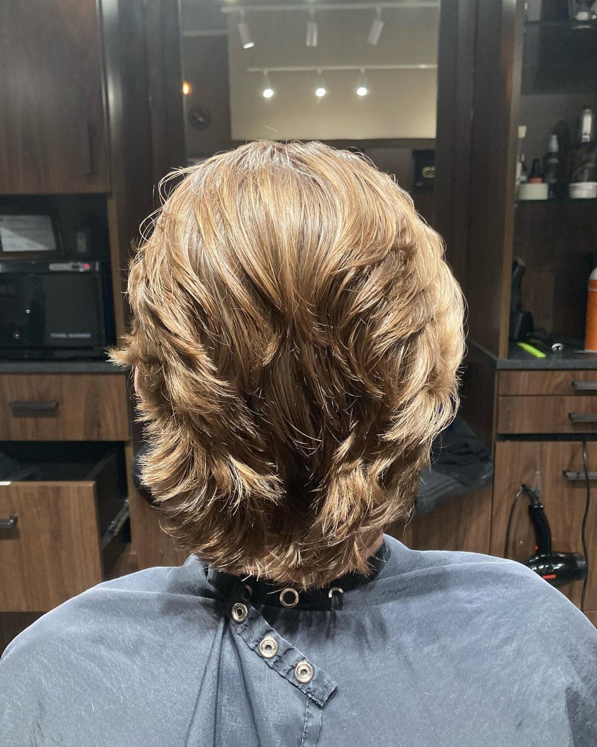 Shoulder-length light brown hair with heavy layers flicking outward in a salon setting.