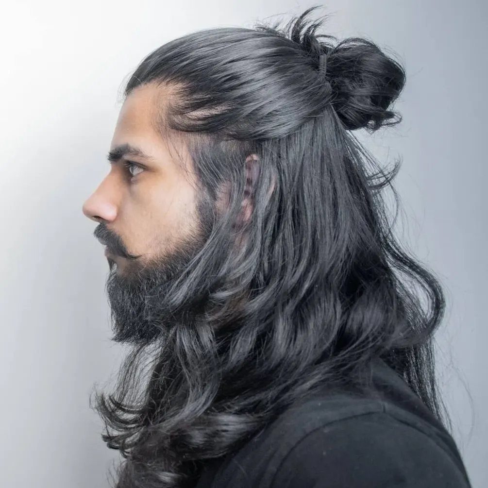 Man with long wavy black hair styled in a half-up man bun and beard.