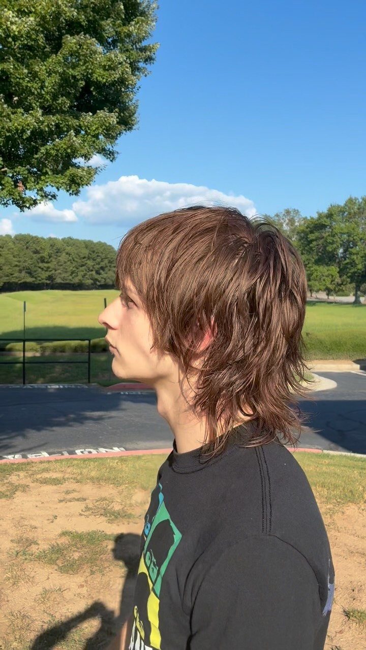 Young man with long brown layered hair and bangs in a side profile