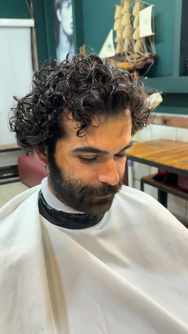 Man with voluminous dark curly hair and a full beard in a barbershop