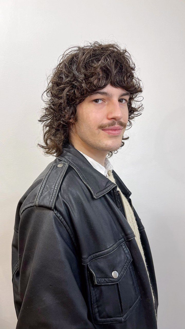 Man with long curly brown hair and mustache wearing a black leather jacket.