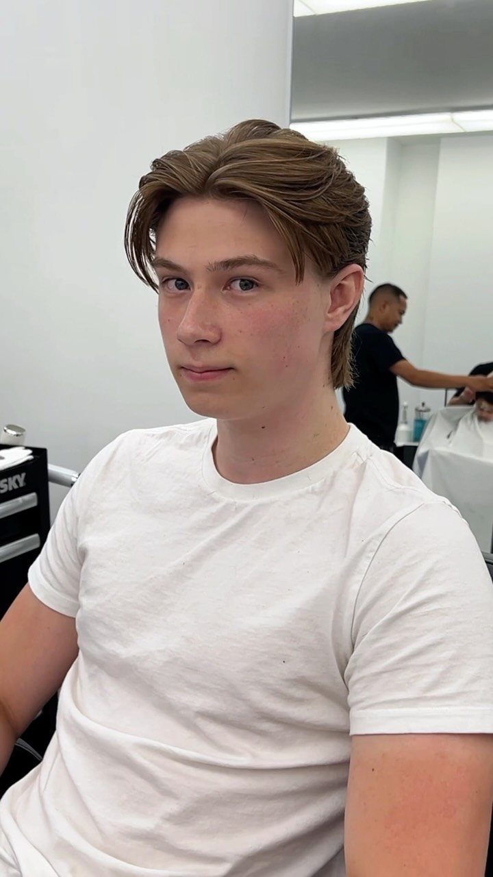Young man with medium-length light brown hair swept back in a barbershop.