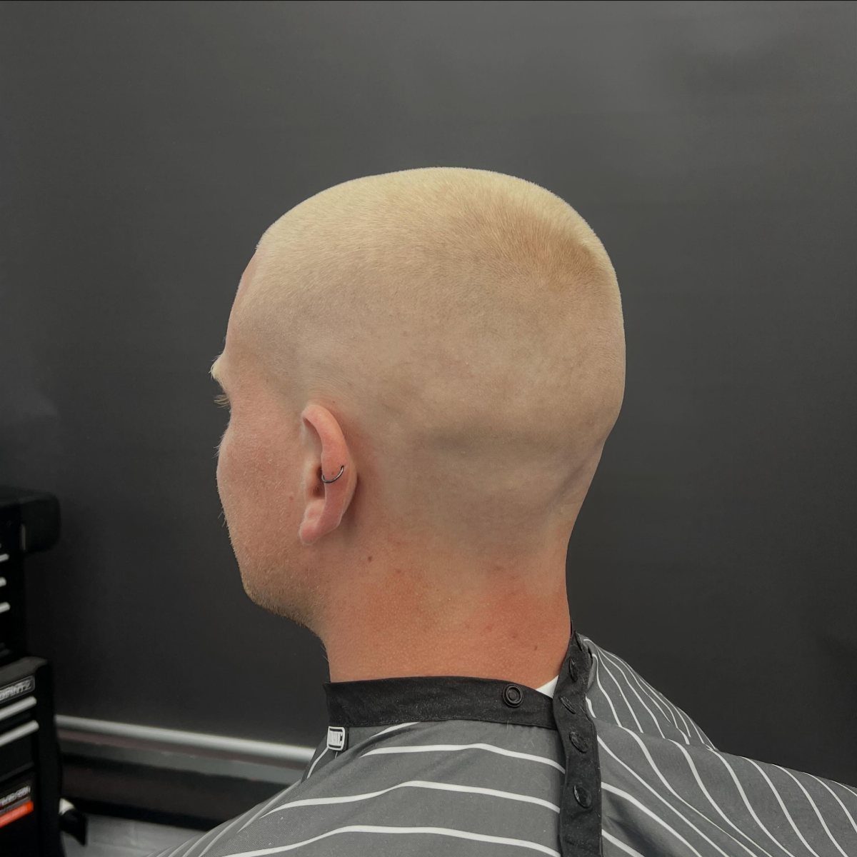 Man with a blonde buzz cut wearing a striped barber cape in a salon.