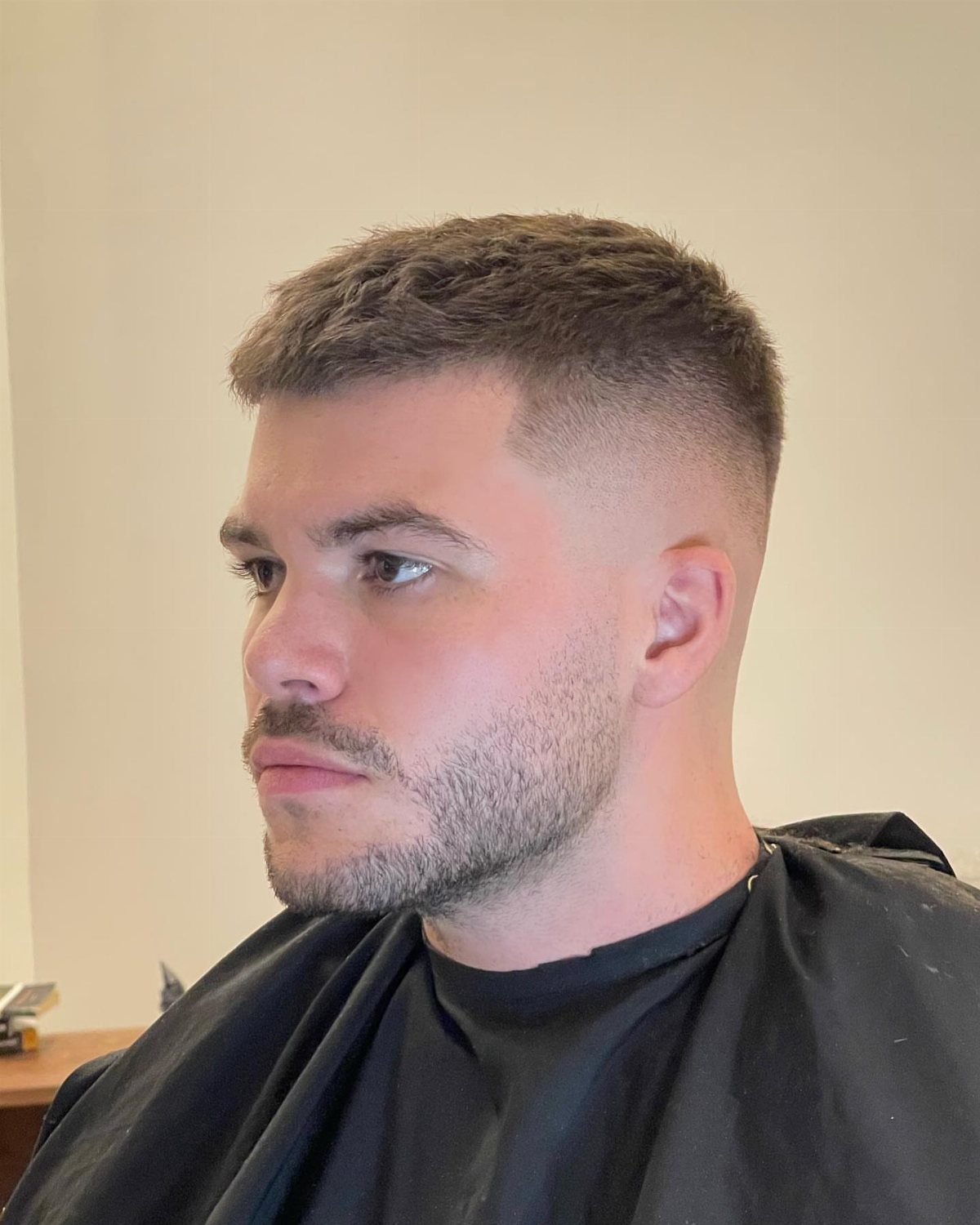 Man with a short crew cut and faded sides wearing a barber cape.