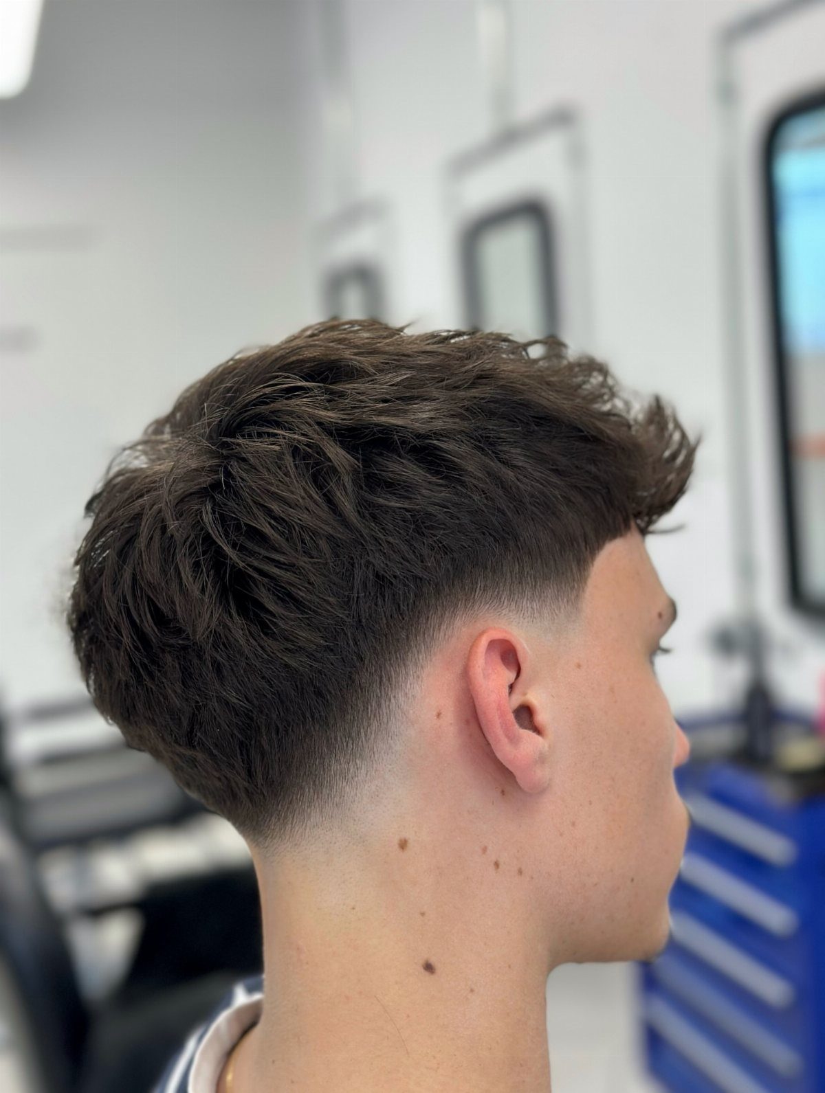 Young man with a brown fade haircut and textured length on top.