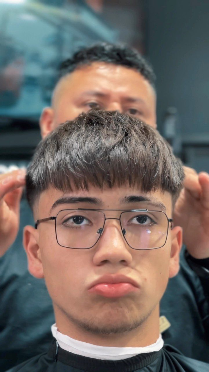 Young man with glasses sporting a textured French crop haircut with a forward fringe.