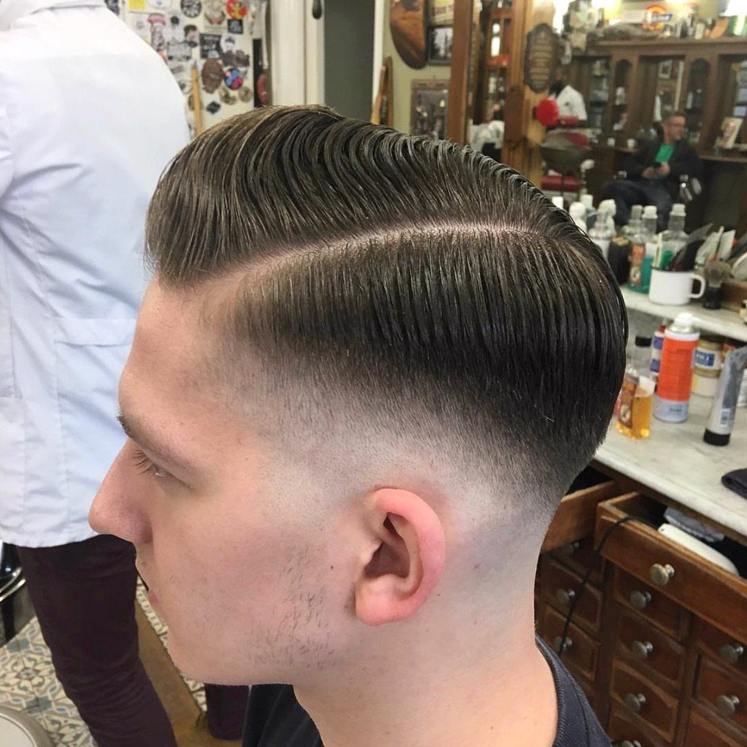 Man with a brown pompadour haircut, hard part, and high skin fade.