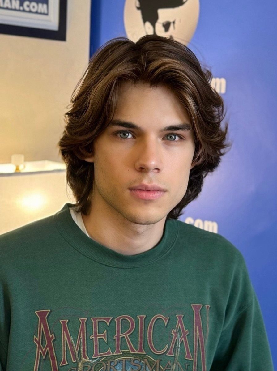 Young man with layered brown hair and blue eyes wearing a green sweatshirt.