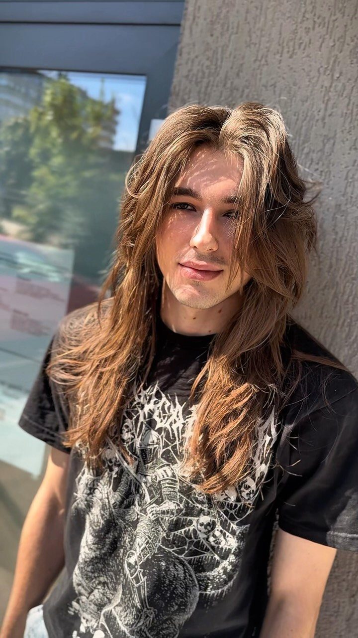 Young man with long straight brown hair wearing a black graphic t-shirt.
