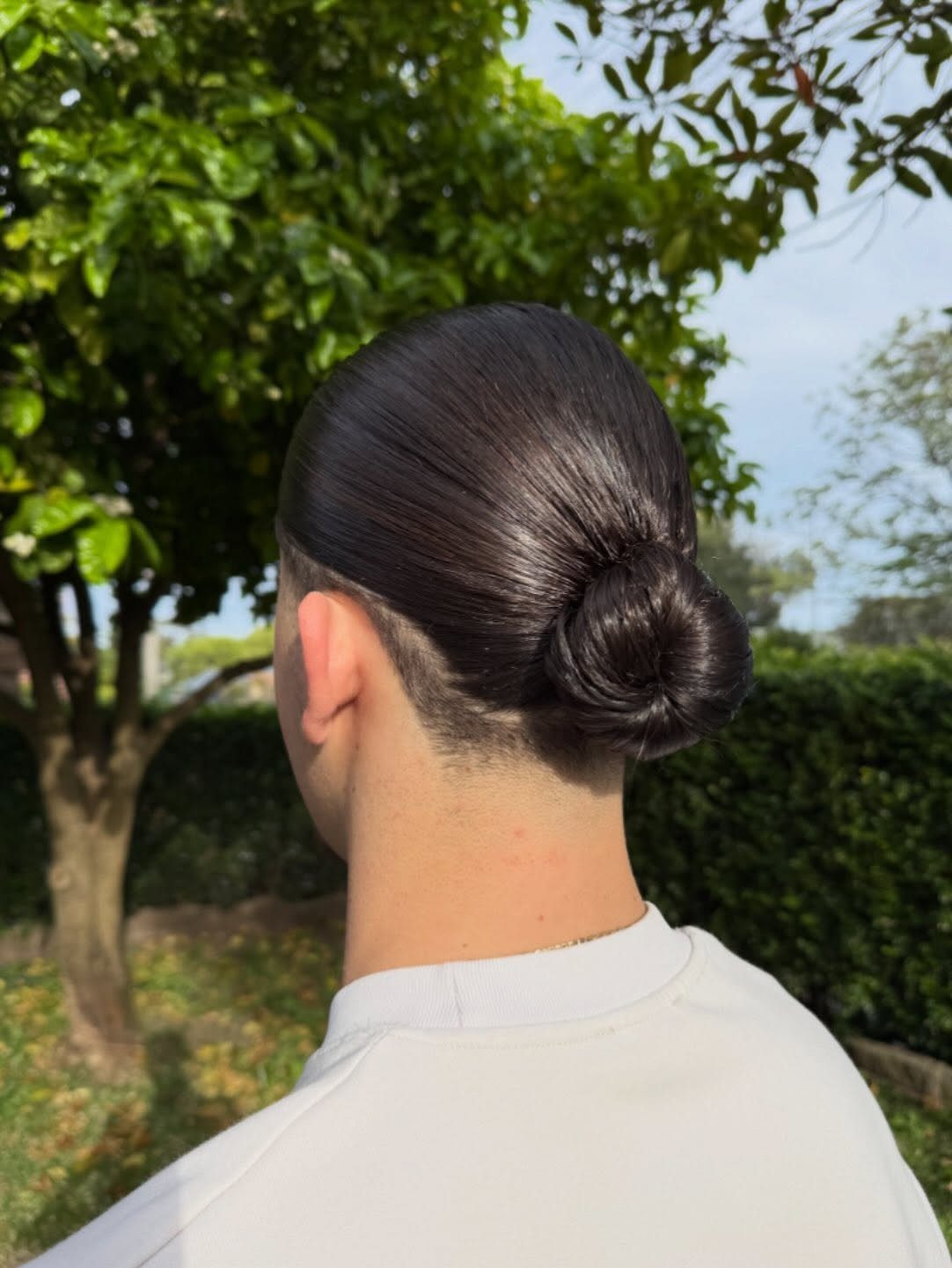 Man with dark straight hair tied into a neat man bun outdoors.