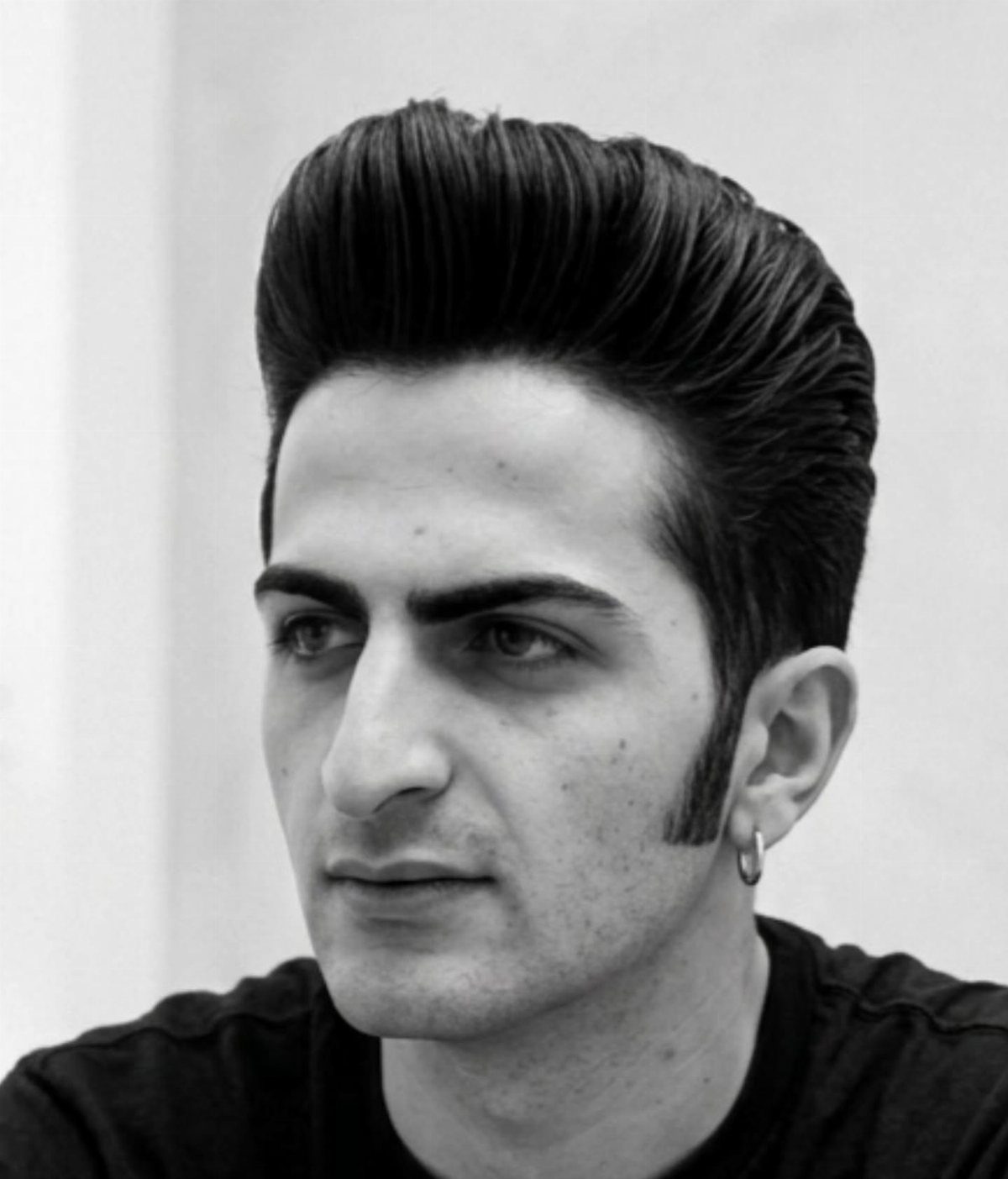 Man with a high-volume pompadour hairstyle and long sideburns in black and white.