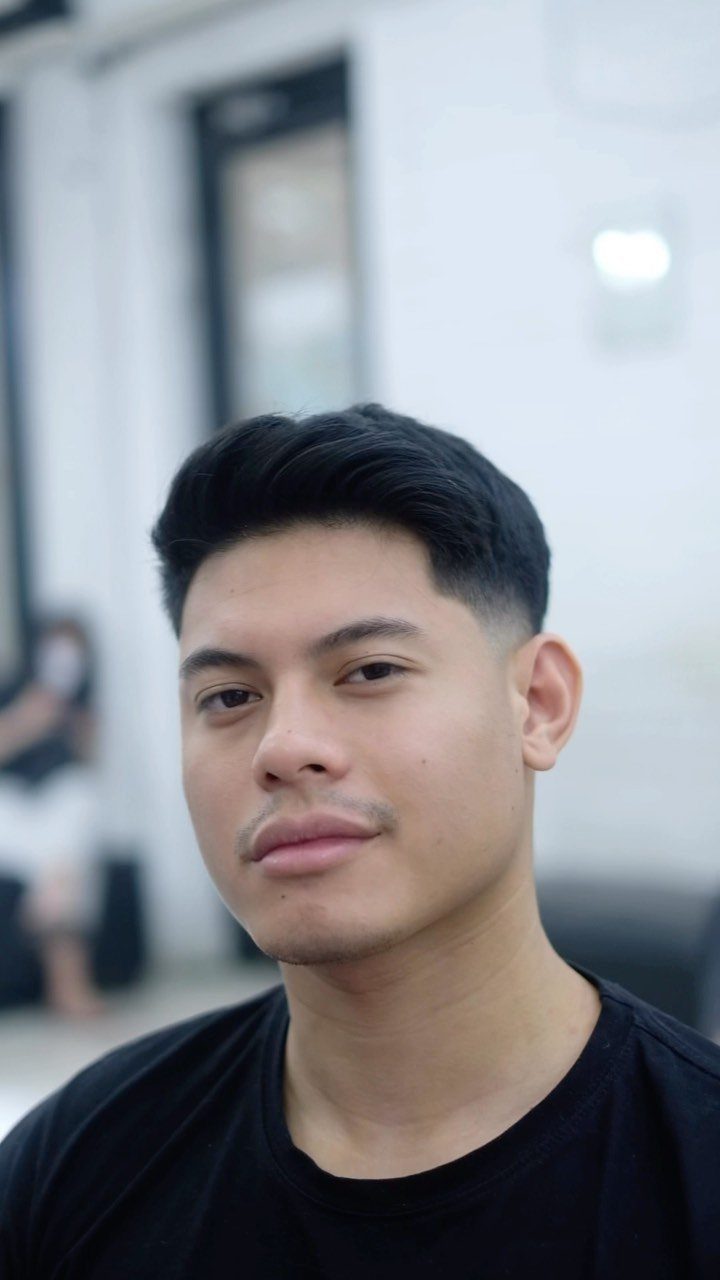 Young man with a dark quiff haircut and faded sides wearing a black shirt.