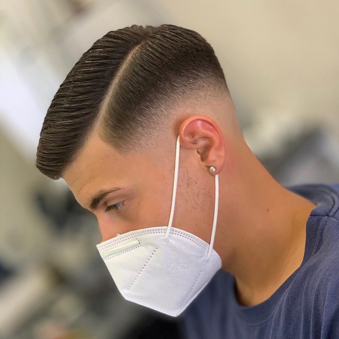 Man with a clean side part haircut and high skin fade wearing a mask.