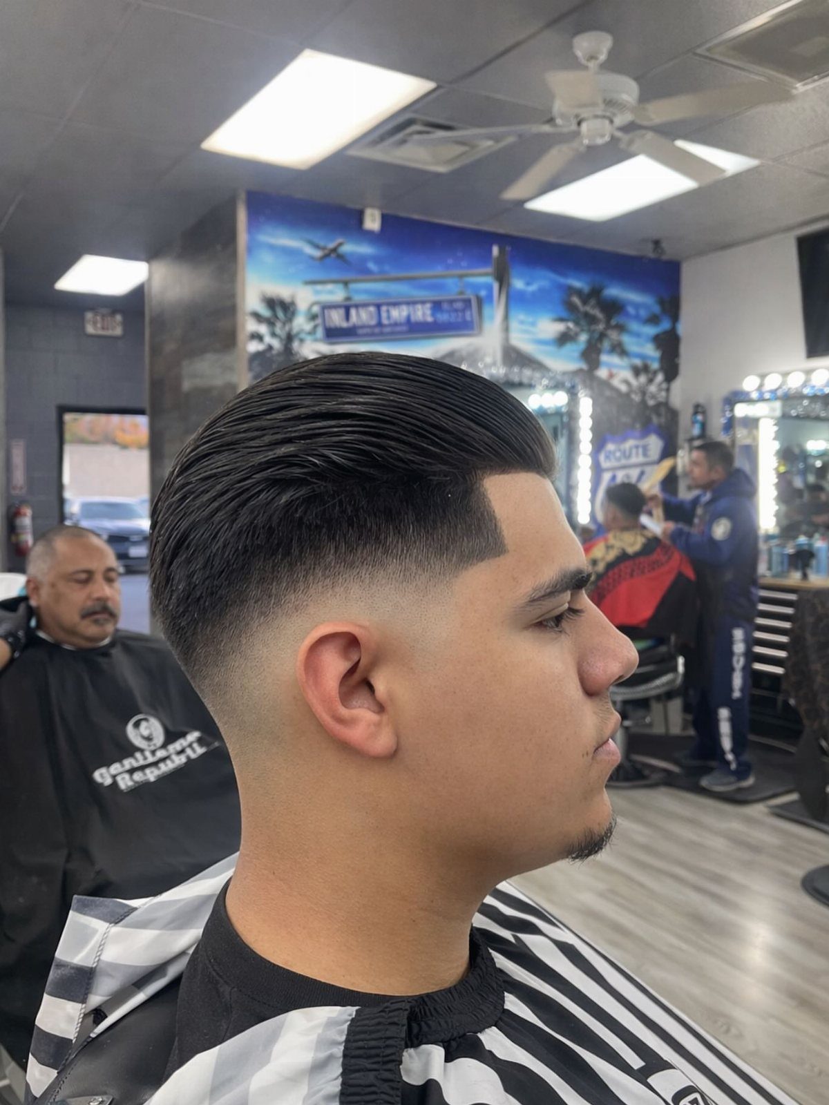 Man with a slicked-back hairstyle and high skin fade in a barbershop.