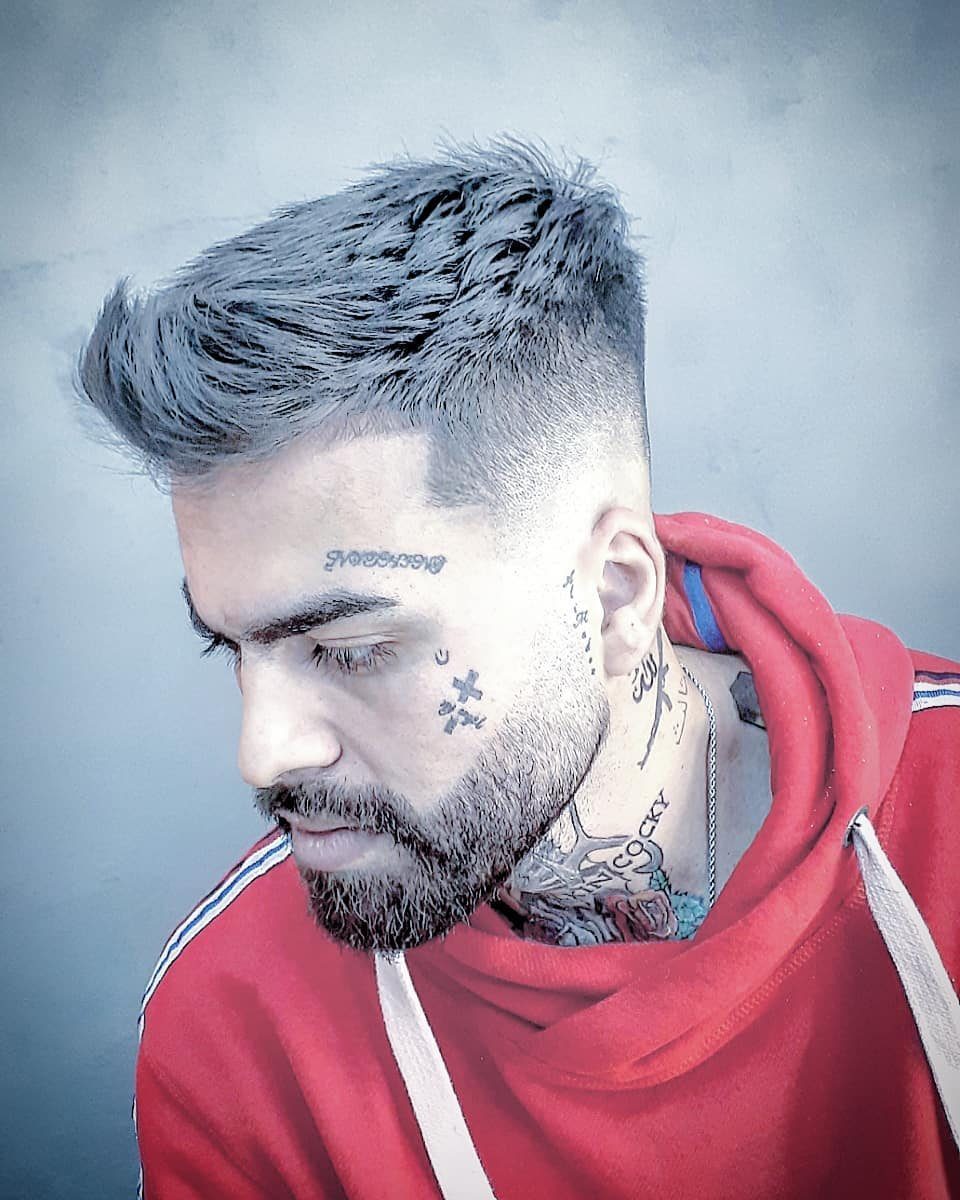 Man with grey spiky hair, a faded undercut, and facial tattoos wearing red hoodie.