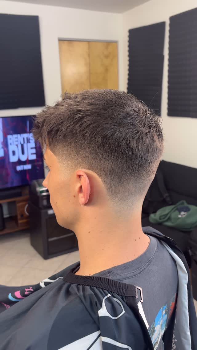 Young man with a skin fade haircut and textured top wearing a barber cape