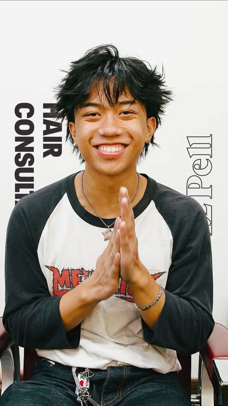 Young man with a choppy black textured shag haircut smiling and posing.