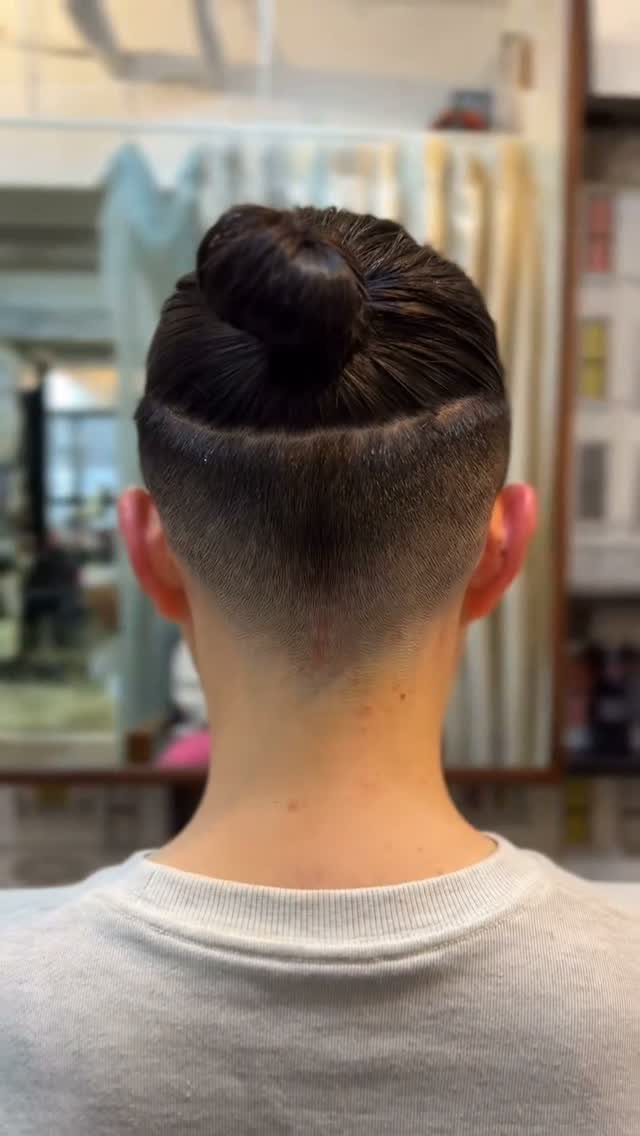 Man with straight dark hair in a top knot and high skin fade.