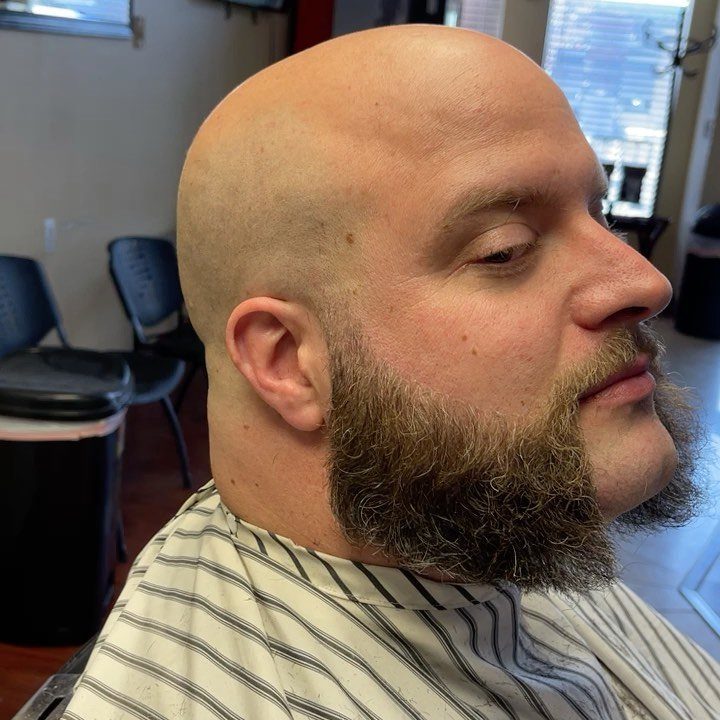 Bald man with a full brown beard wearing a striped barber cape.