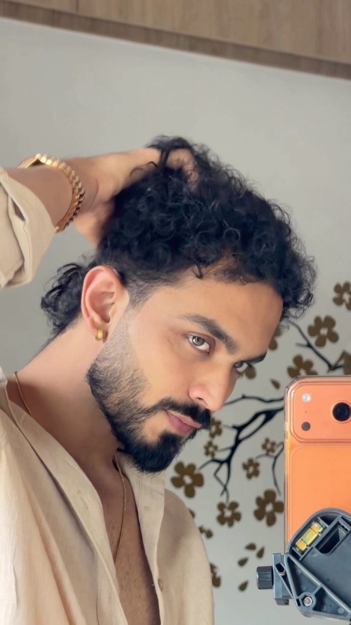 Man with curly black hair and a groomed beard posing for a mirror selfie.