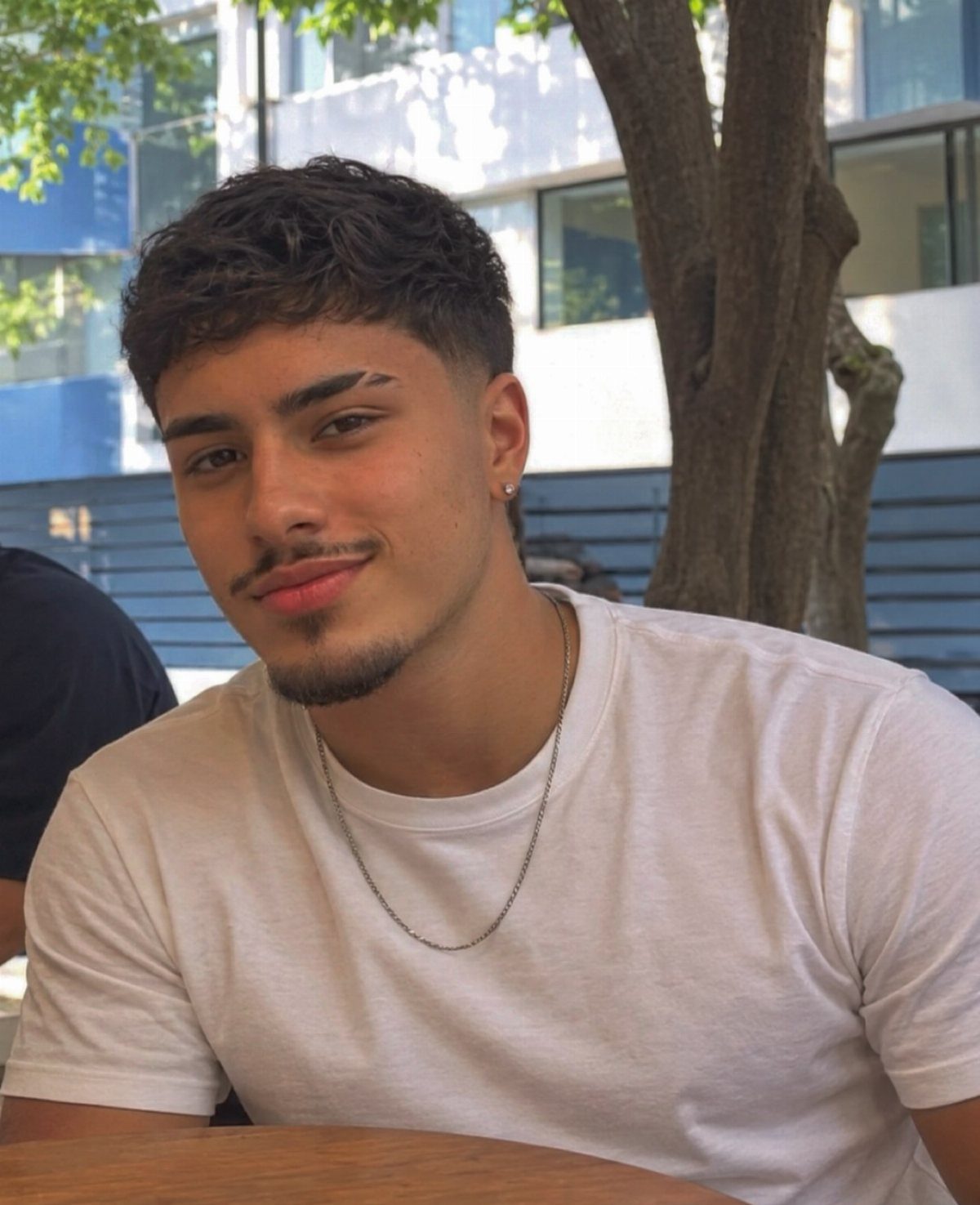 Young man with a textured fade haircut and groomed beard wearing a white t-shirt.