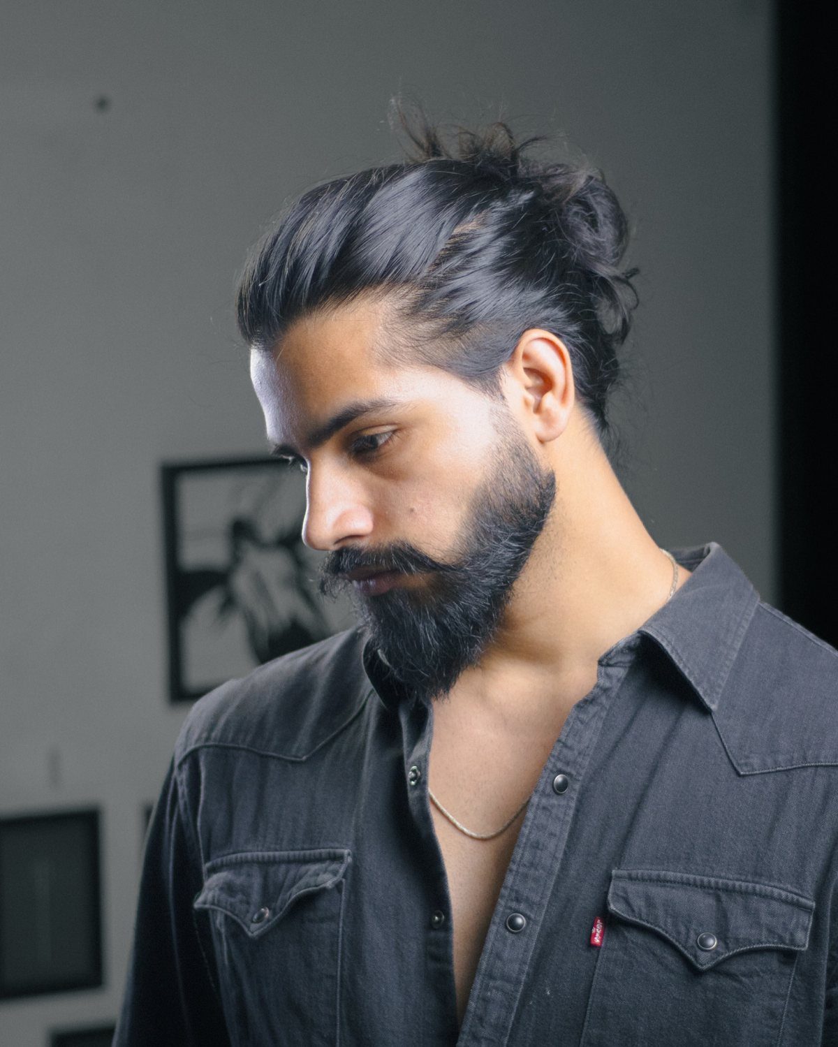 Man with a dark man bun and a full groomed black beard wearing grey shirt.