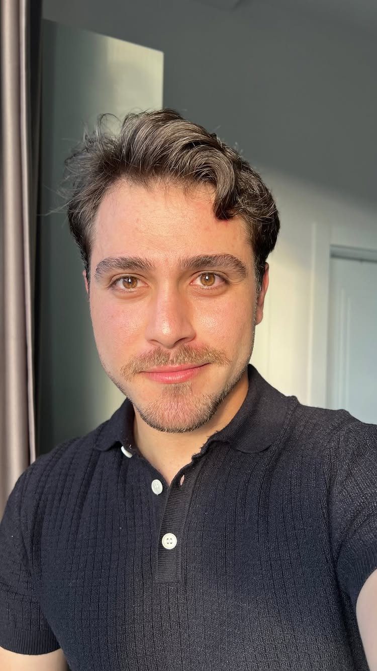 Man with brown hair and light facial hair wearing a black polo shirt.