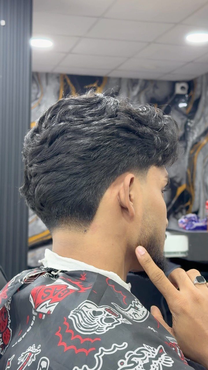 Man with wavy dark hair and a taper fade blended into a beard.