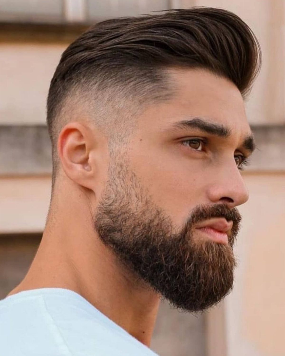 Man with a brown undercut hairstyle and a full groomed beard in profile.