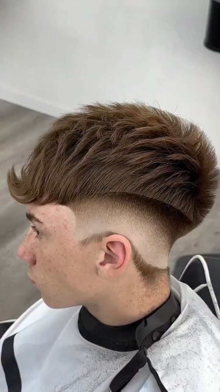 Young man with a brown burst fade haircut and textured top in a barbershop.