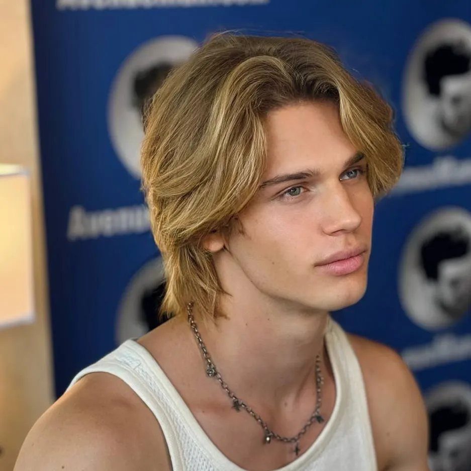 Young man with blonde hair in a middle-parted curtain haircut and white tank top.