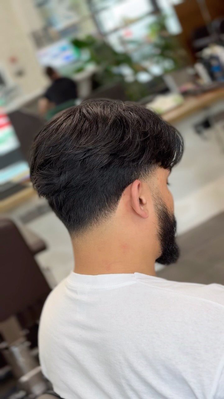 Man with a dark drop fade haircut and beard in a barbershop.