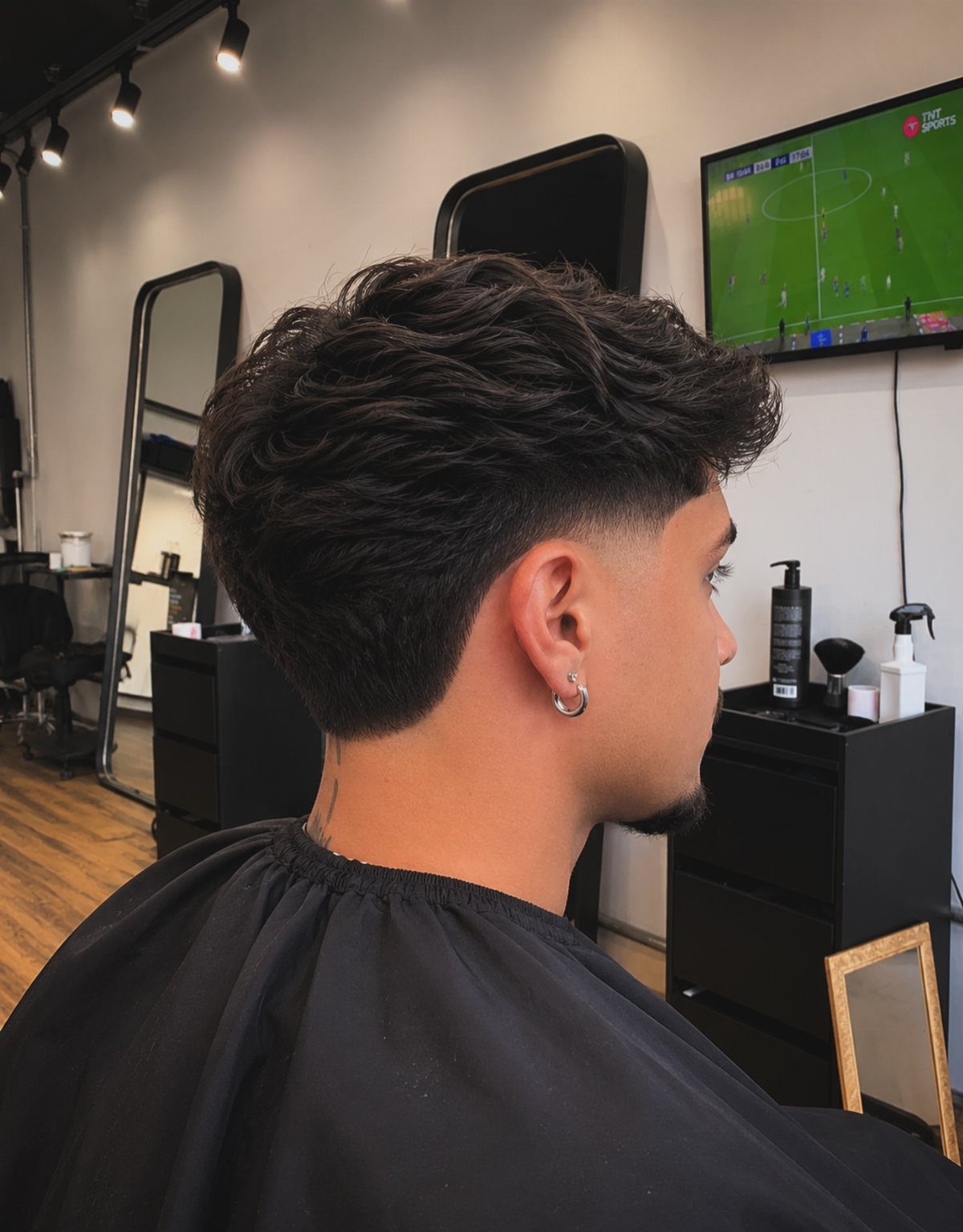 Man with wavy dark hair and a low taper fade in a barbershop