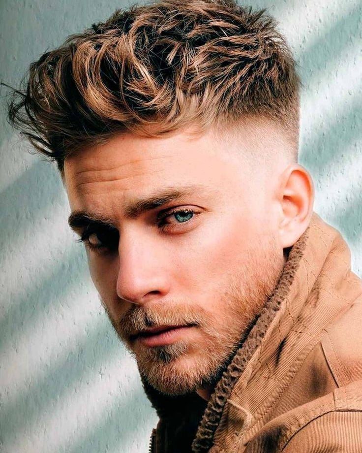 Man with a textured messy hairstyle and high skin fade wearing a brown jacket.