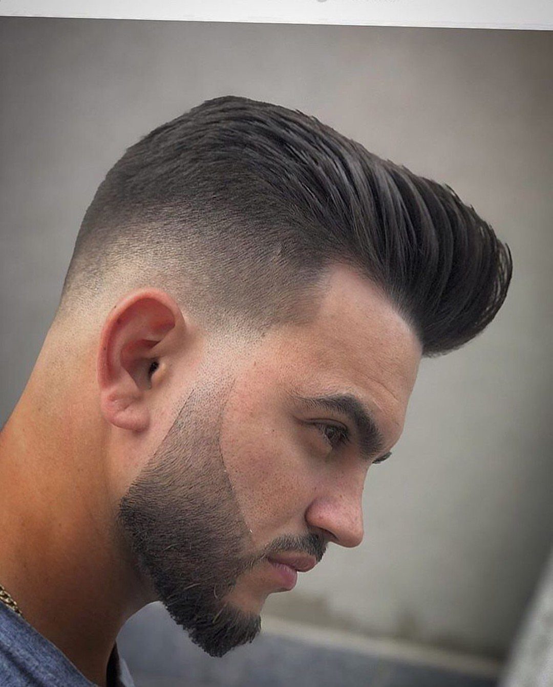 Man with a high-volume pompadour haircut and a clean skin fade on sides.