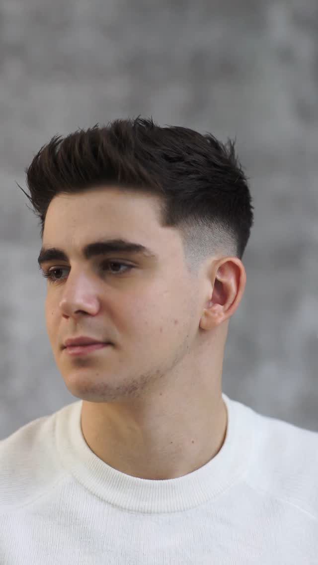 Young man with a quiff haircut and faded sides against a grey wall
