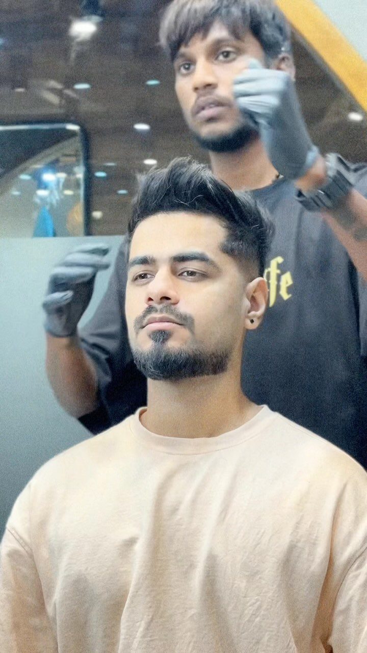 Man with a faux hawk hairstyle being styled by a barber in a salon.