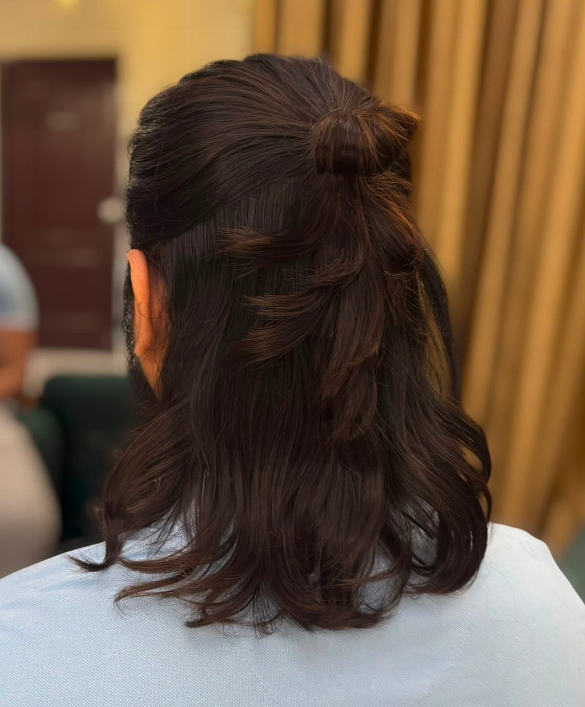 Man with long dark brown hair tied in a half-up man bun hairstyle.