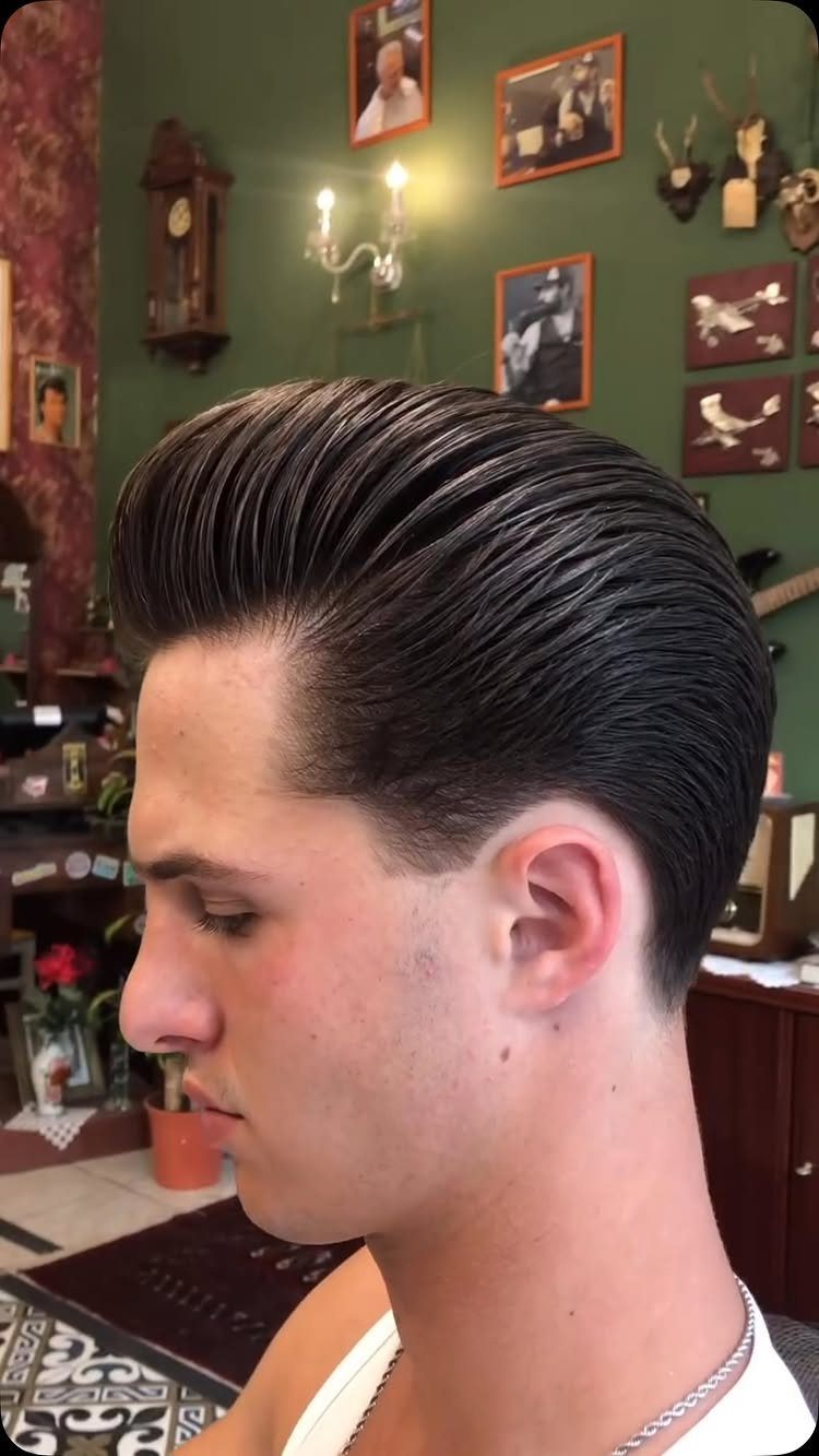 Young man with a high-volume, slicked-back pompadour hairstyle in a room with green walls.