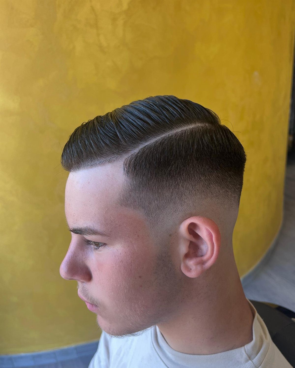 Young man with a clean side part hairstyle and faded sides against yellow wall