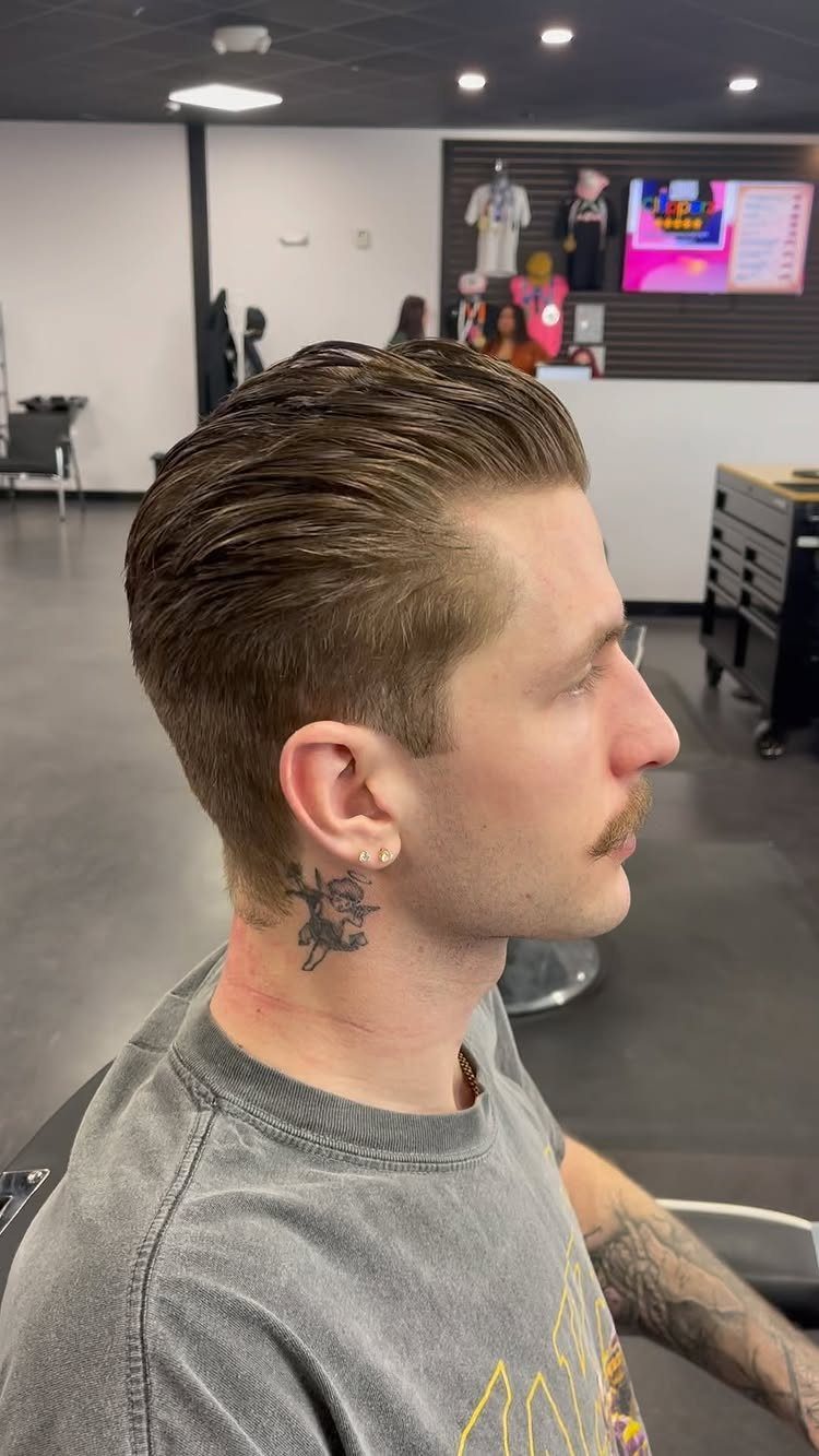 Man with straight brown hair styled slicked-back in a professional barbershop setting.