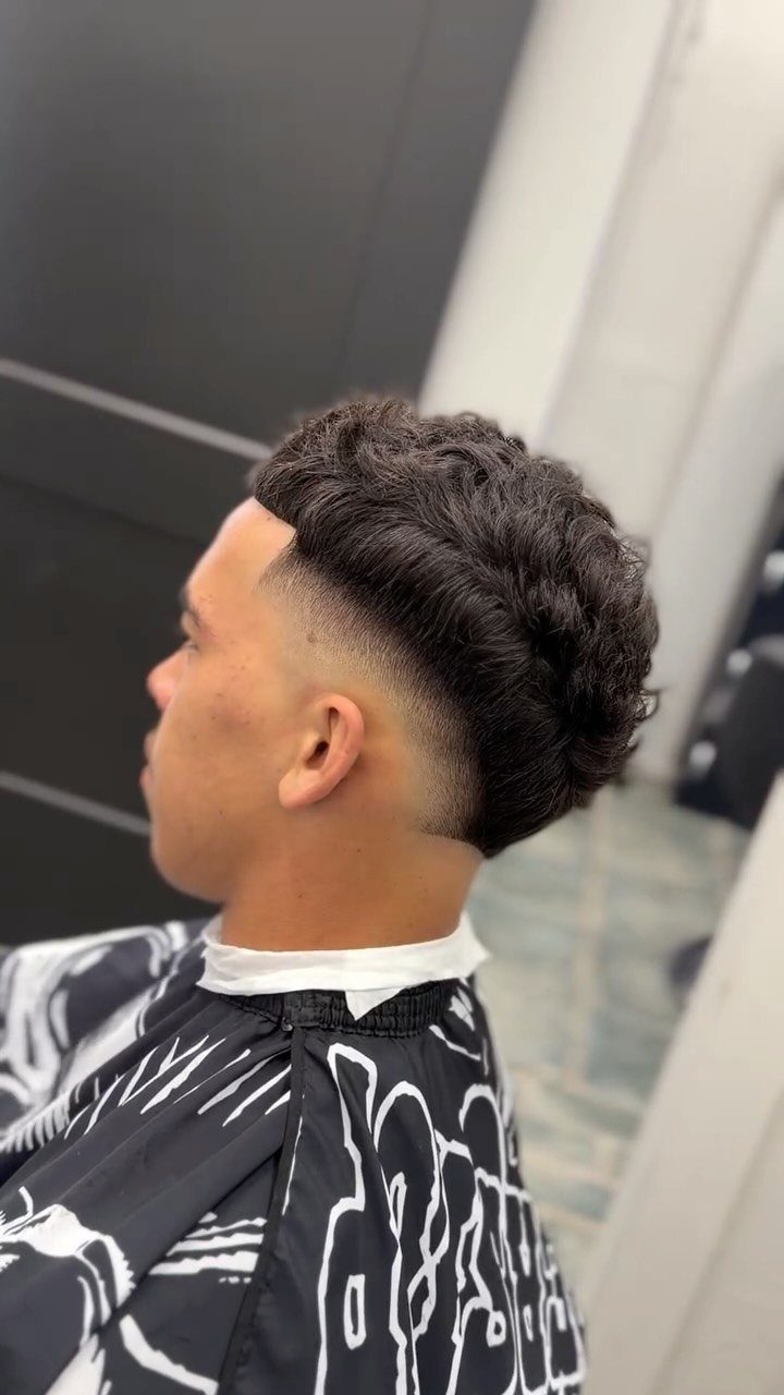 Man with curly hair featuring a high burst fade haircut and barber cape.