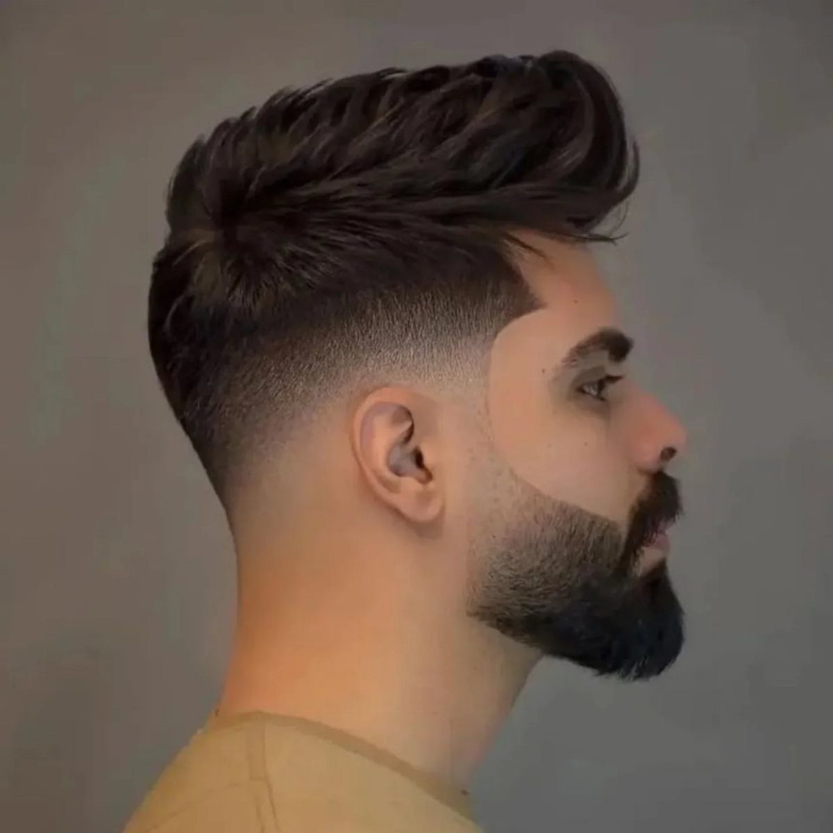 Man with a high fade haircut and hair brushed up with a groomed beard.