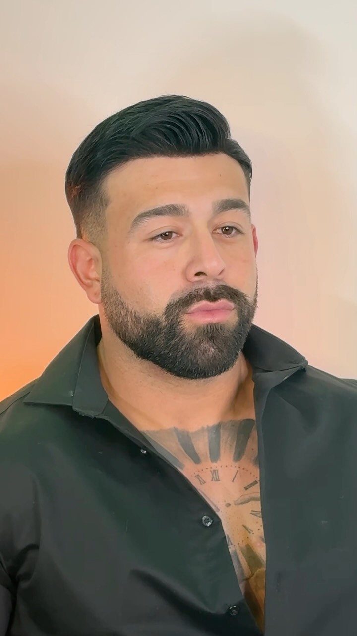 Man with a high fade comb-over haircut and a full groomed beard.
